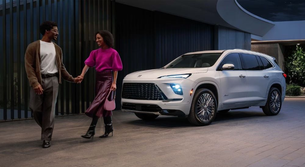 A couple holding hands walking away from a white 2027 Buick Enclave Avenir