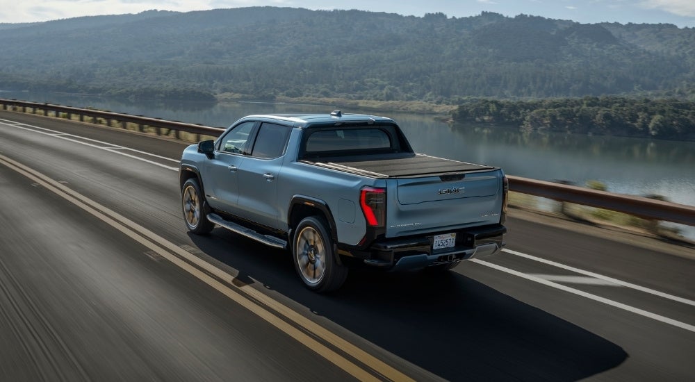 A blue 2025 GMC Sierra EV Denali driving on a highway.