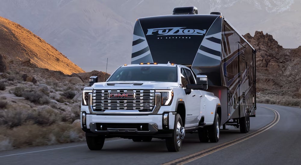 A white 2024 GMC Sierra 3500 HD Denali Dually towing a large RV.