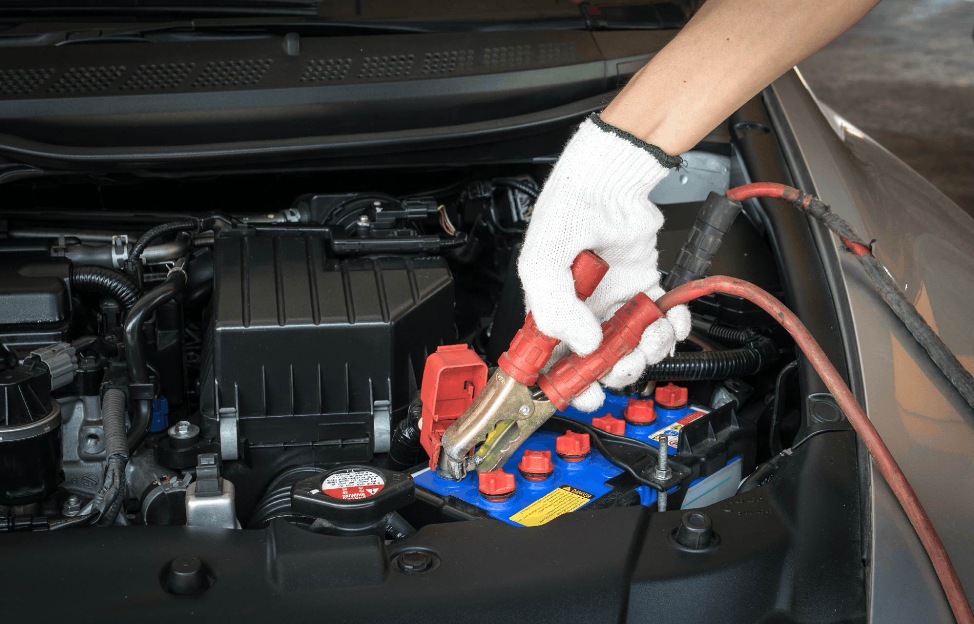 Technician connecting a jumper cable to a car battery during Kia battery service