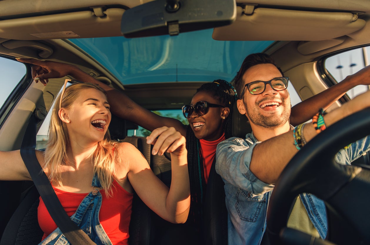 Two young women and a young man smiling while driving in a car on a summer day