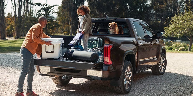 A father and daughter onload camping supplies from the bed of a black Toyota Tundra.