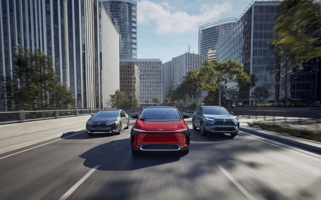 Three Toyota vehicles driving through a modern city street, featuring a red crossover SUV in the center flanked by a sedan and SUV.