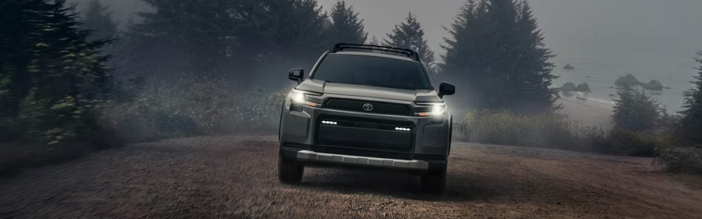 Toyota Hybrid driving on a foggy forest road near the coastline with headlights on, showcasing rugged hybrid performance and adventure-ready capability.
