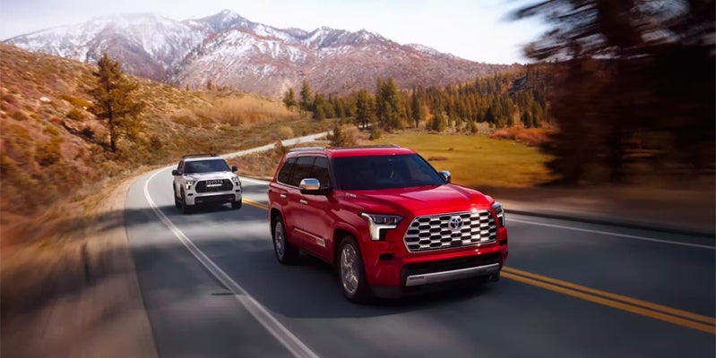 Two Toyota Sequoia's driving down a winding road with mountains in the distance.