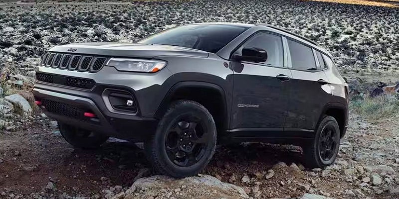 An image of a dark gray metallic Jeep Compass fording rocky terrain.