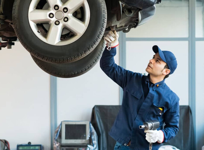 An image of an automotive technician performing 30,000-mile service on a car that is up on a riser. 