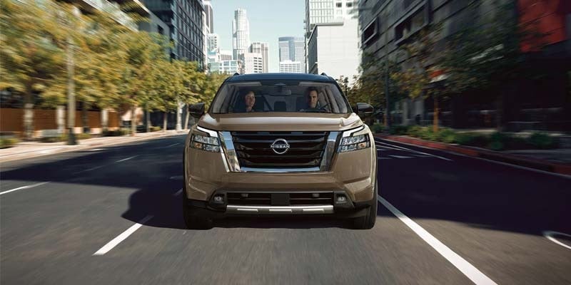 A 2024 Nissan Pathfinder in gold driving towards the camera down a city street.