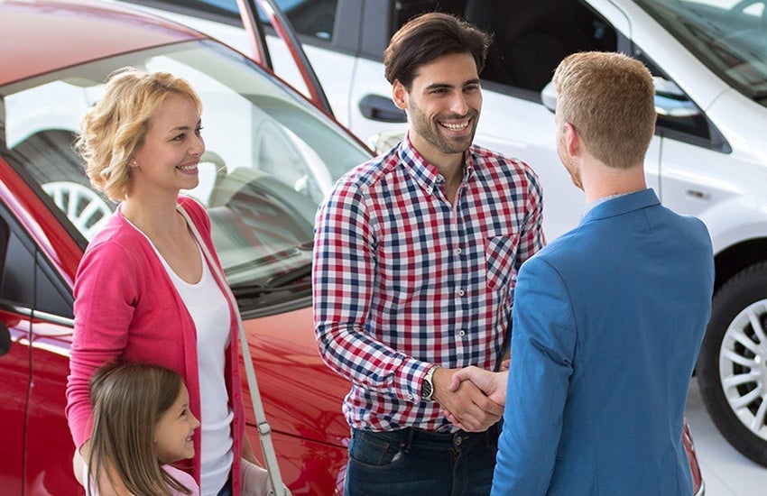 A family shaking hands with a member of the sales team while finalizing the purchase of a new car. 
