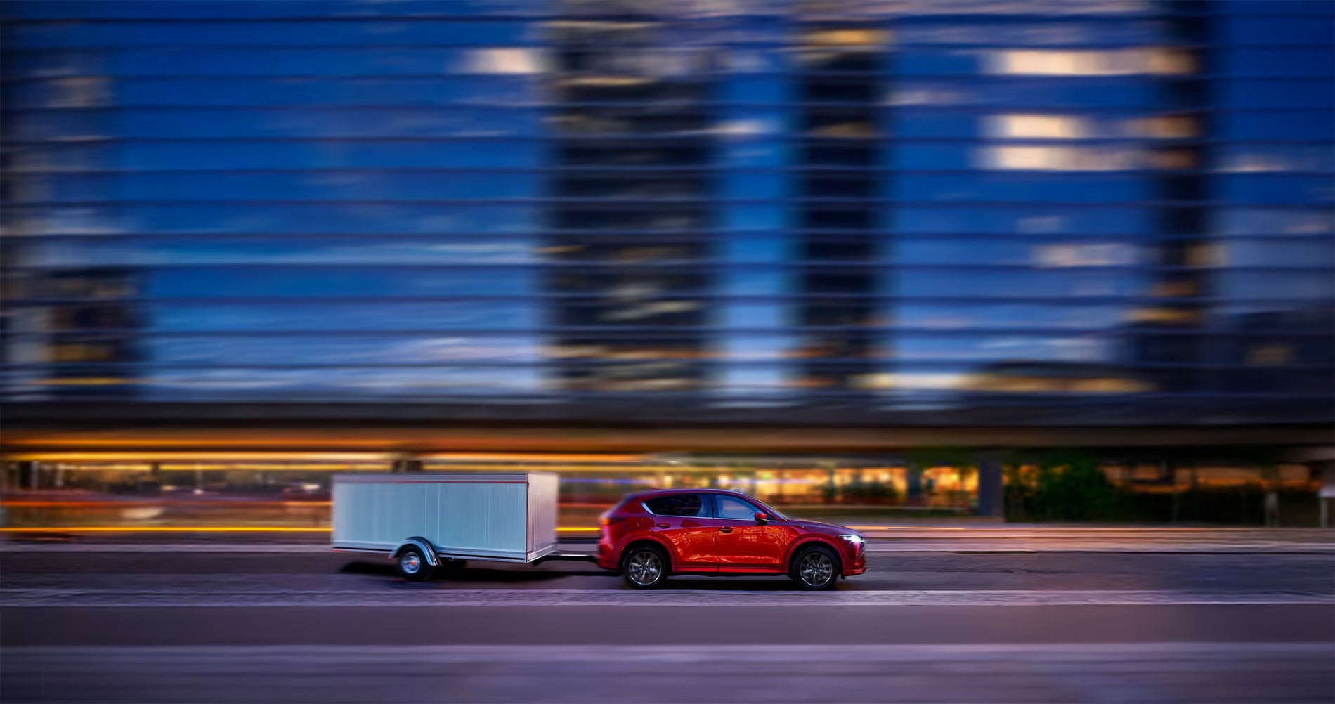 2025-Mazda-CX-5-towing-an-enclosed-trailer-through-dowtown-of-a-city-at-night
