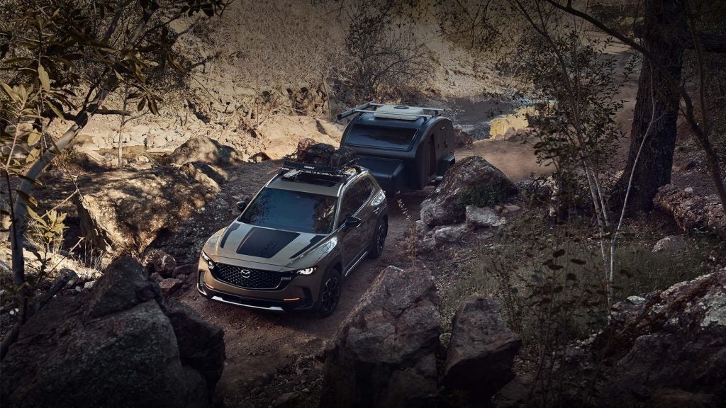 A dark gray Mazda CX-50, shot from above, towing a trailer, with a black racing stripe up its hood.
