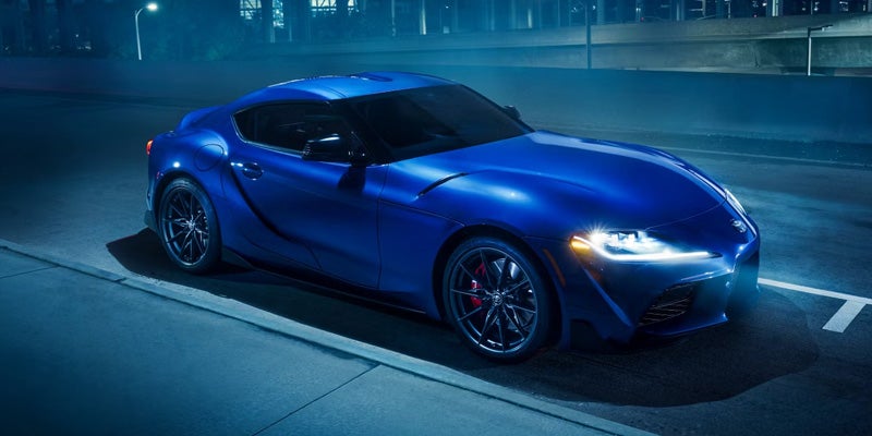 Blue 2025 Toyota GR Supra parked at night on a city street, reflecting streetlights.