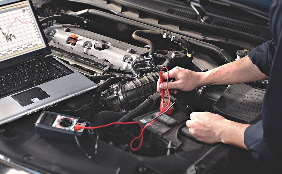 A technician checking a car battery for functionality. 