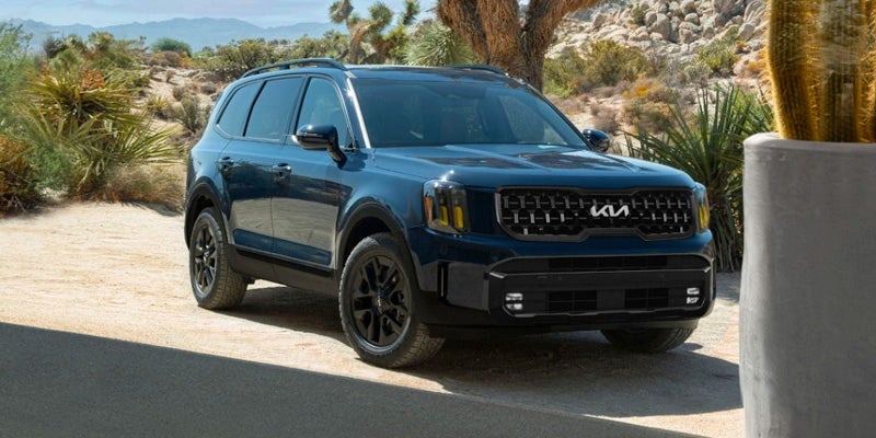 A black Kia Telluride backed by a sand dune covered in scrubgrass and mountains on the horizon. 