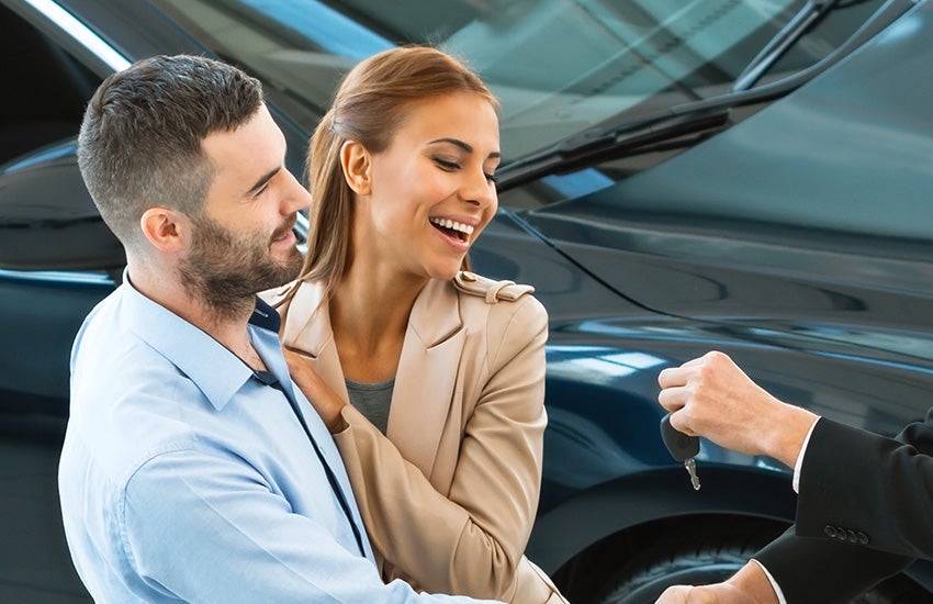 A happy young couple receiving the keys to their new car after a successful dealership financing agreement.