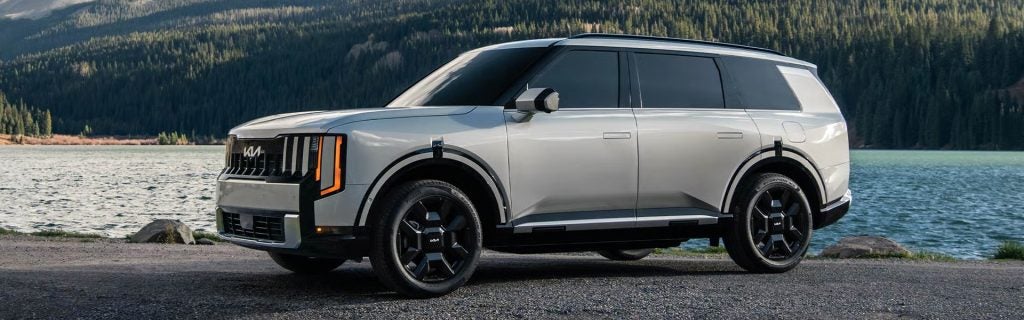 Silver Kia SUV parked by a lake with mountains in the background
