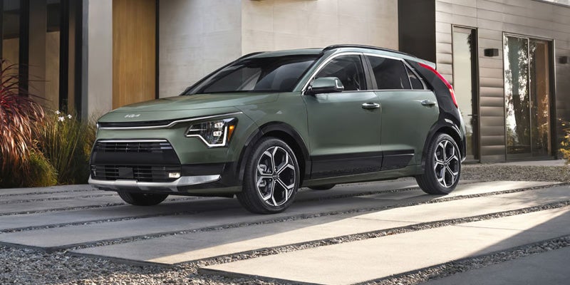 A green compact SUV with black fender trim is angled towards the viewer on a modern stone driveway.