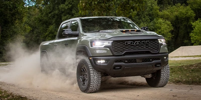 A Ram 1500 pickup truck leaving a trail of dust driving on a dirt road.