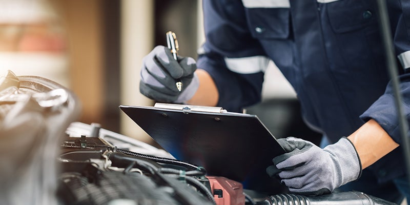 A service technician reviewing a checklist from a clipboard while inspecting a vehicle's engine.