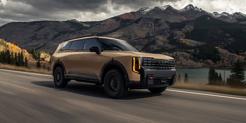 A Kia Telluride on the road driving by a mountain.
