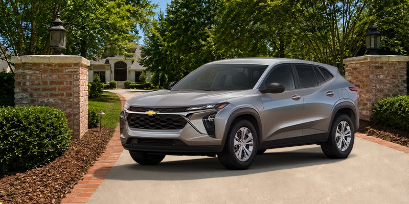 A Sterling Gray Metallic Chevrolet Trax compact SUV parked on a paved driveway in front of a house.