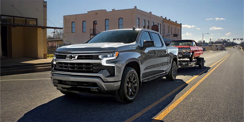 A 2026 Chevrolet Silverado 1500 towing a vintage car behind it.
