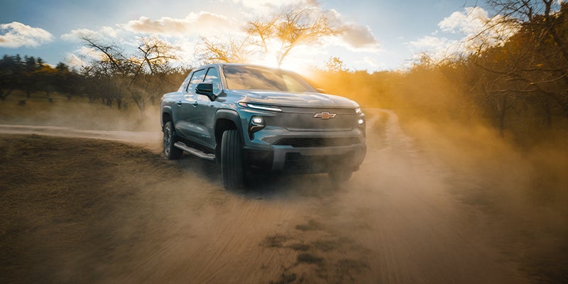 A Chevrolet Silverado EV driving off-road through a dusty dirt road.
