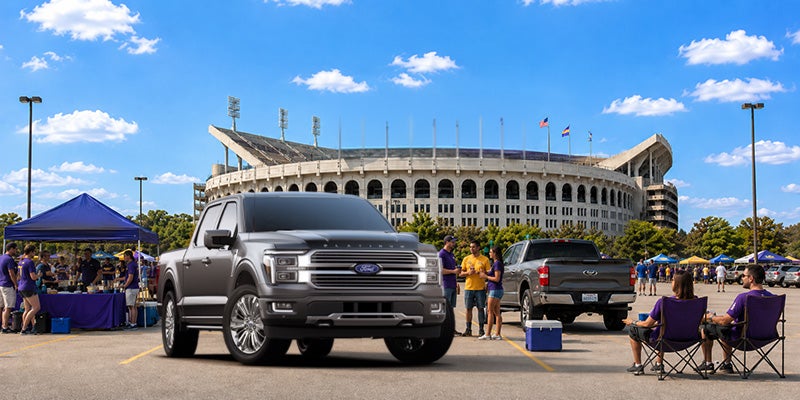 A grey Ford F-150 Platinum featuring a bold chrome grille and premium chrome wheels parked at a tailgate event outside a stadium.