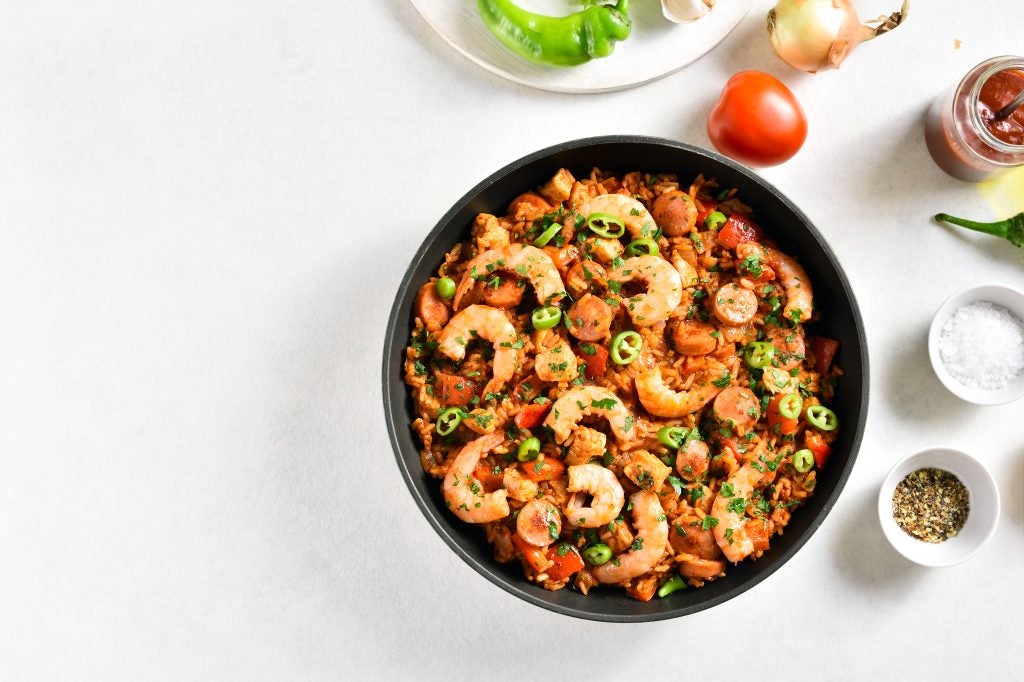 Creole jambalaya with chicken, smoked sausages and vegetables in frying pan on white stone background with copy space. - Genesis of Baton Rouge, LA