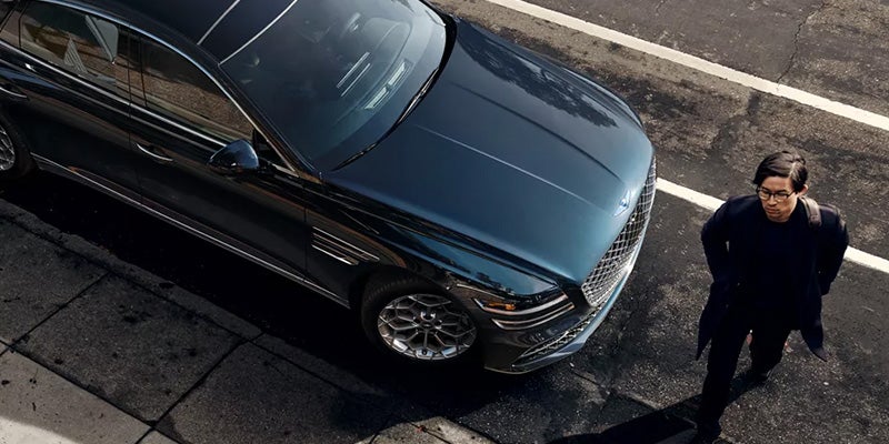 A new jade green 2024 Genesis G80 parked on the side of the street with a person walking in front of it. - Genesis of Baton Rouge, LA
