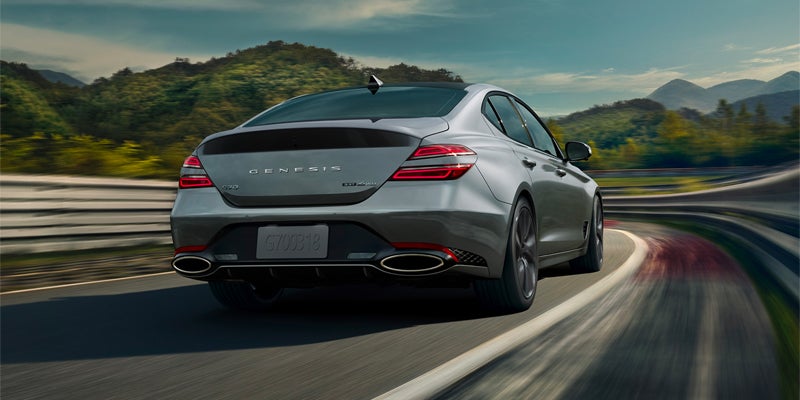 A Silver Genesis sedan driving down on off-ramp among forested hills. - Genesis of Baton Rouge, LA