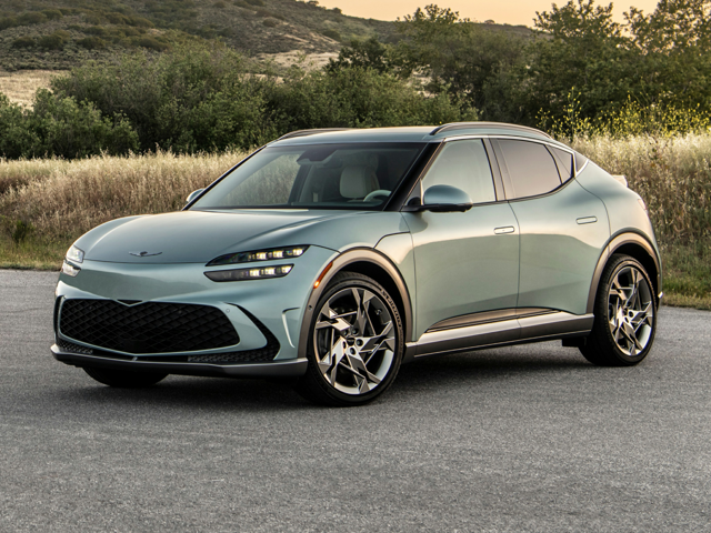 An all-new Brunswick Green Matte Genesis GV60 parked in front of a hill covered in small trees and long grass. - Genesis of Baton Rouge Dealership