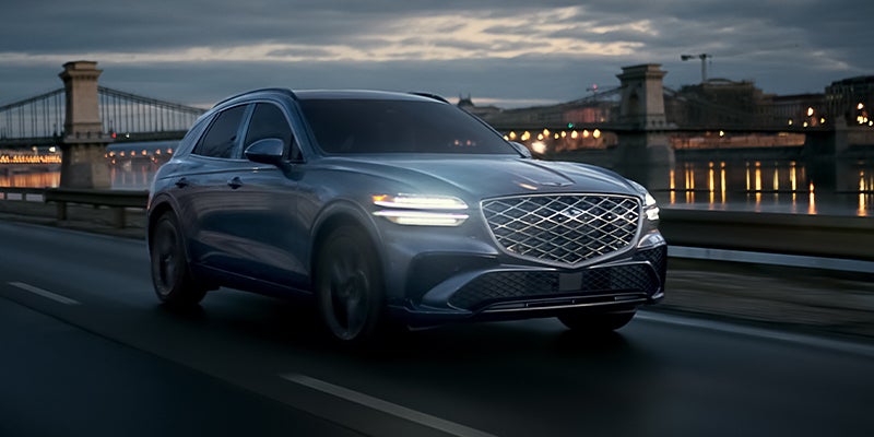 The 2026 Genesis GV70 driving at night with headlights on.