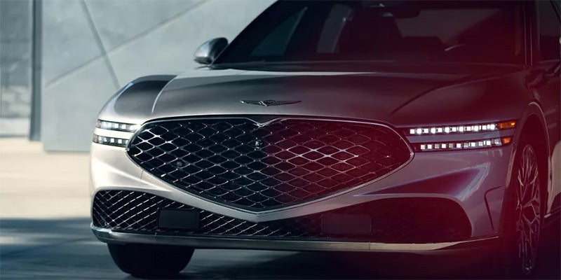 An all-new Savile Silver 2024 Genesis G90 parked underneath a car port in front of a modern building. - Genesis of Baton Rouge, LA