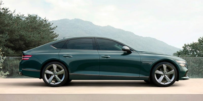An all-new 2024 Emerald Green Genesis G80 parked among the rolling hills of trees. - Genesis of Baton Rouge, LA