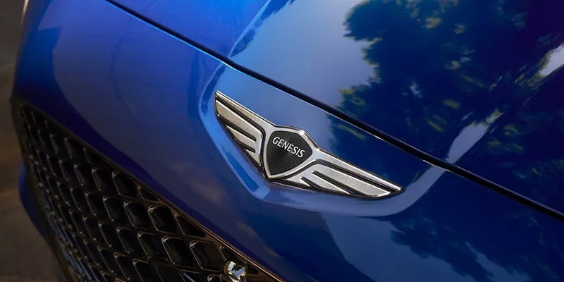 The front emblem of a blue 2024 Genesis vehicle. - Genesis of Baton Rouge, LA