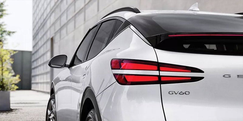 An all-new white 2025 Genesis GV60 parked in front of a modern concrete structure. - Genesis of Baton Rouge, LA