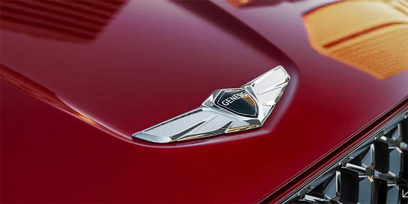 A close up picture of the Genesis hood emblem on a red Genesis GV70. - Genesis of Baton Rouge, LA