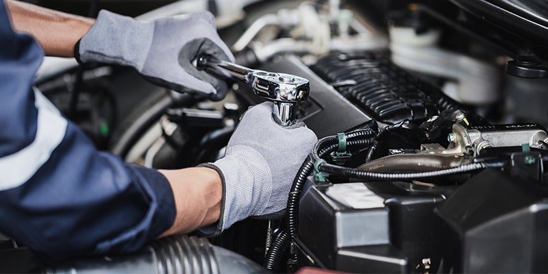 A close-up of a service technician performing maintenance service on a vehicle's engine.