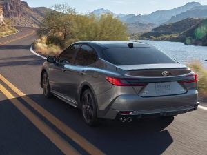 2026 Toyota Camry Hybrid driving on a two lane road in the country.