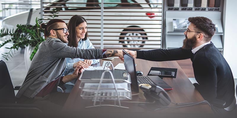 Couple sitting in an office shaking hands with sales person.
