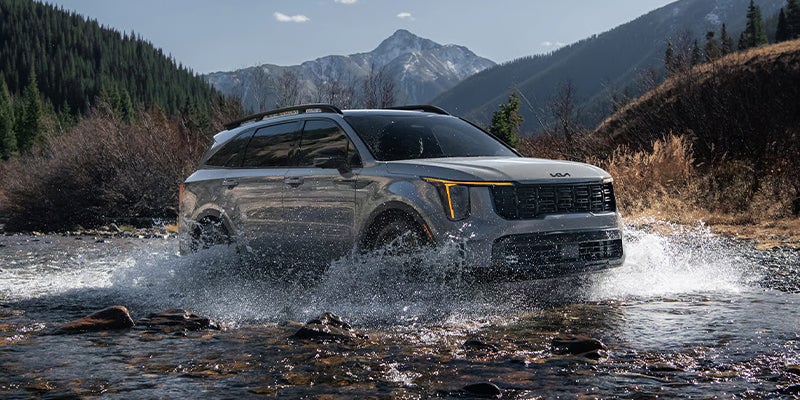 A silver Kia Sorento SUV traversing shallow water.