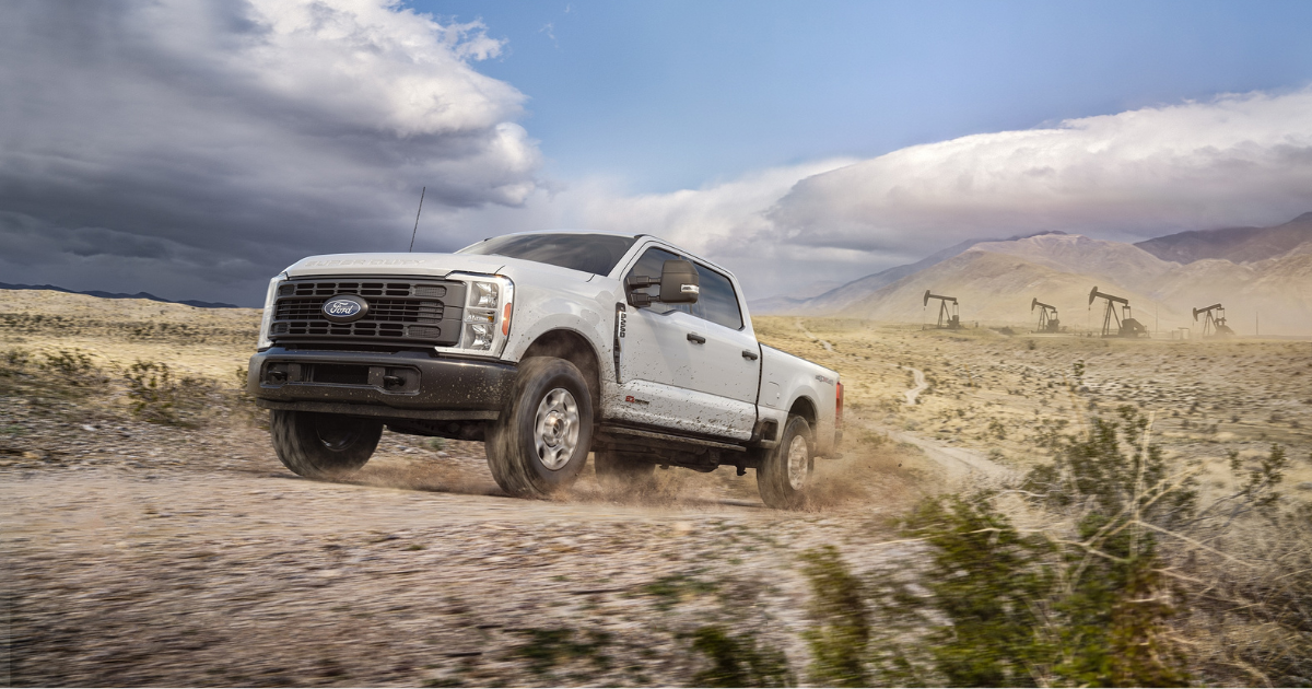 a 2027 Ford Super Duty driving in the back roads with oil fields to the right