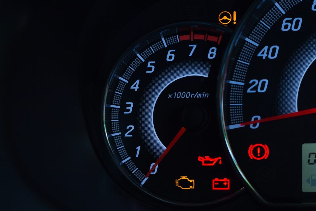 A close-up of a car's digital dashboard at night, showing the tachometer and several illuminated warning lights, including engine, battery, and oil pressure.
