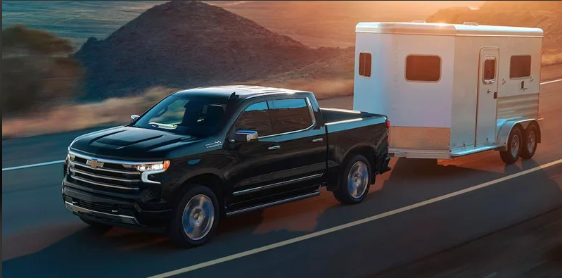 a black 2024 Chevy Silverado 1500 towing a trailer down the road near Lawrence, MA.