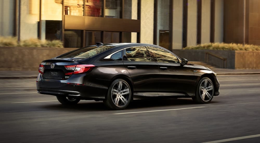One of many hybrid cars for sale, a black 2021 Honda Accord Hybrid, driving on a city street.