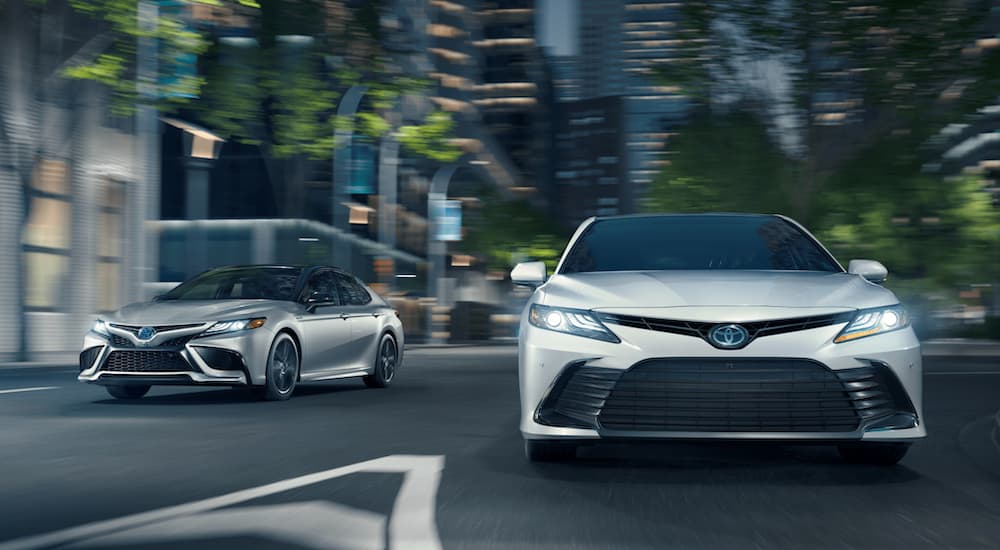 A white and a silver 2021 Toyota Camry driving through a city intersection at night.