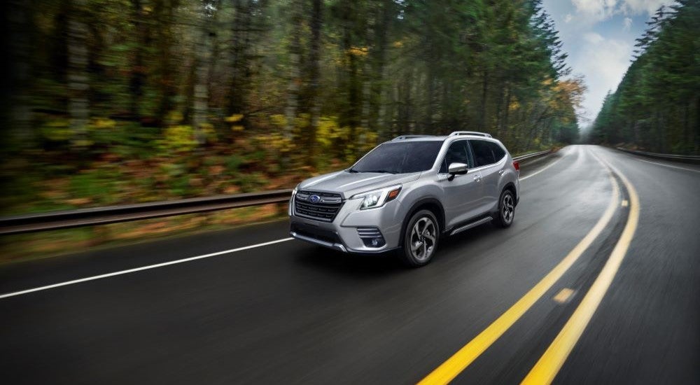 A silver 2023 Subaru Forester driving by trees.