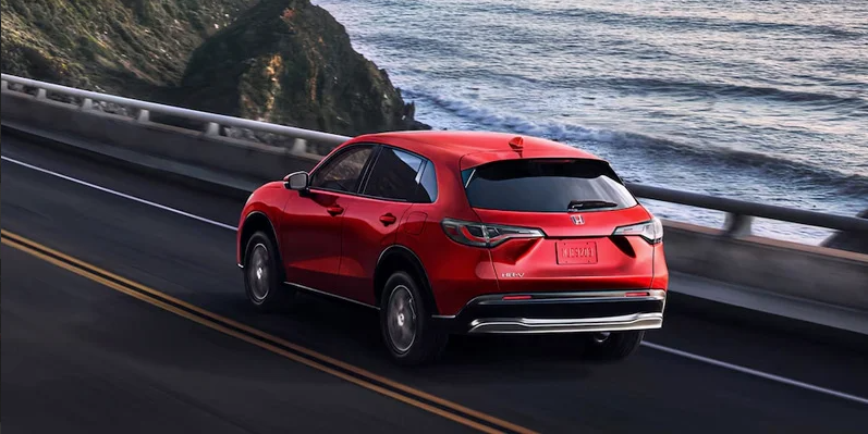 A red 2025 Honda HR-V driving along the coast.