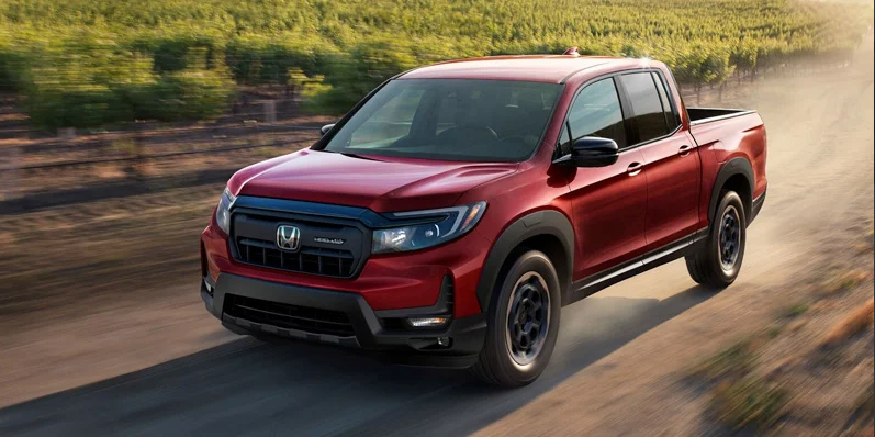 A red 2025 Honda Ridgeline driving down a dirt road.